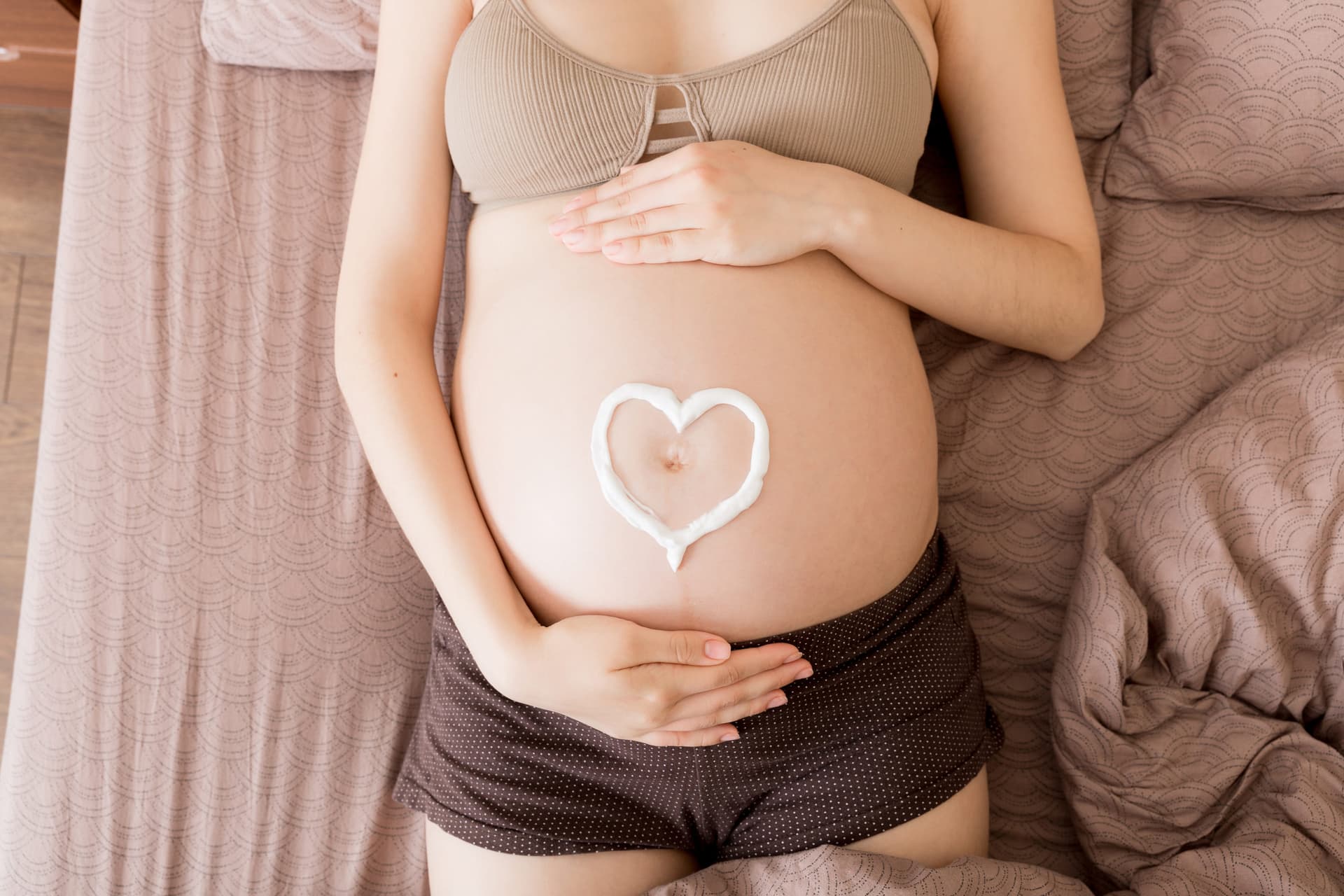 Pregnant woman relaxing on her bed at home with a heart drawn in lotion on her belly