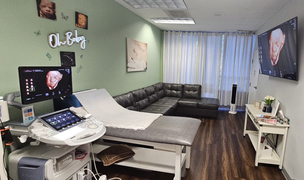Video Prenatal ultrasound room in Charlotte with a Voluson system, exam bed, guest sofa and large wall screen